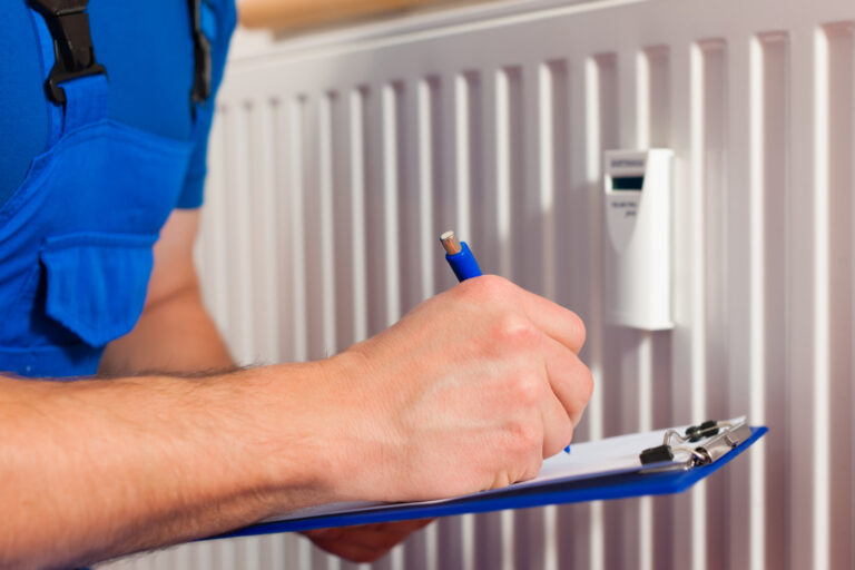 A man in blue overalls writes on a clipboard, engaged in inspecting heating system
