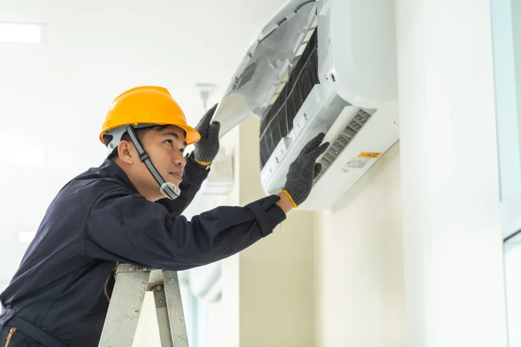 AC Service in Poway, CA 1 A man in a hard hat and safety glasses repairs an air conditioner.